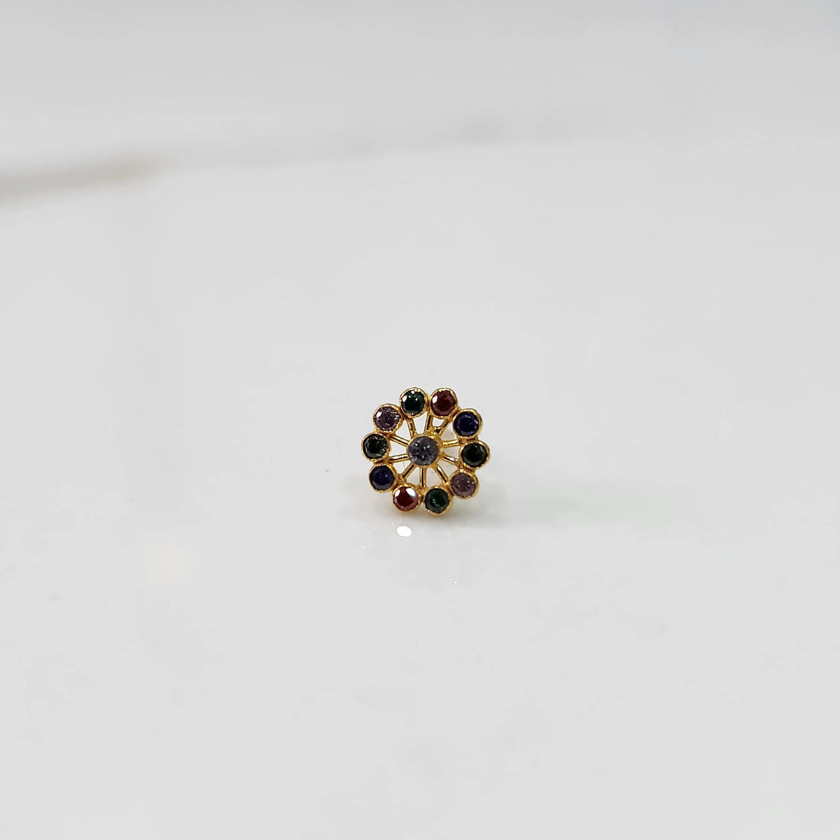 Front view of large gold nose pin with multicolor gemstone flower ring design on white background
