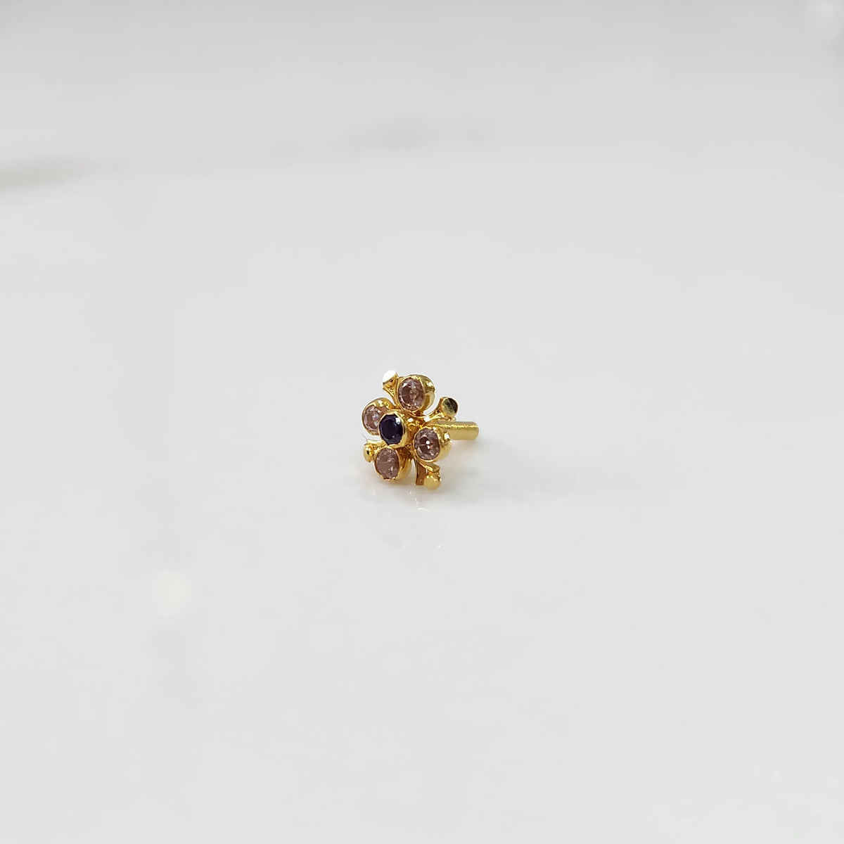 Side angle view of gold nose pin with multicolor gemstone flower design on white background