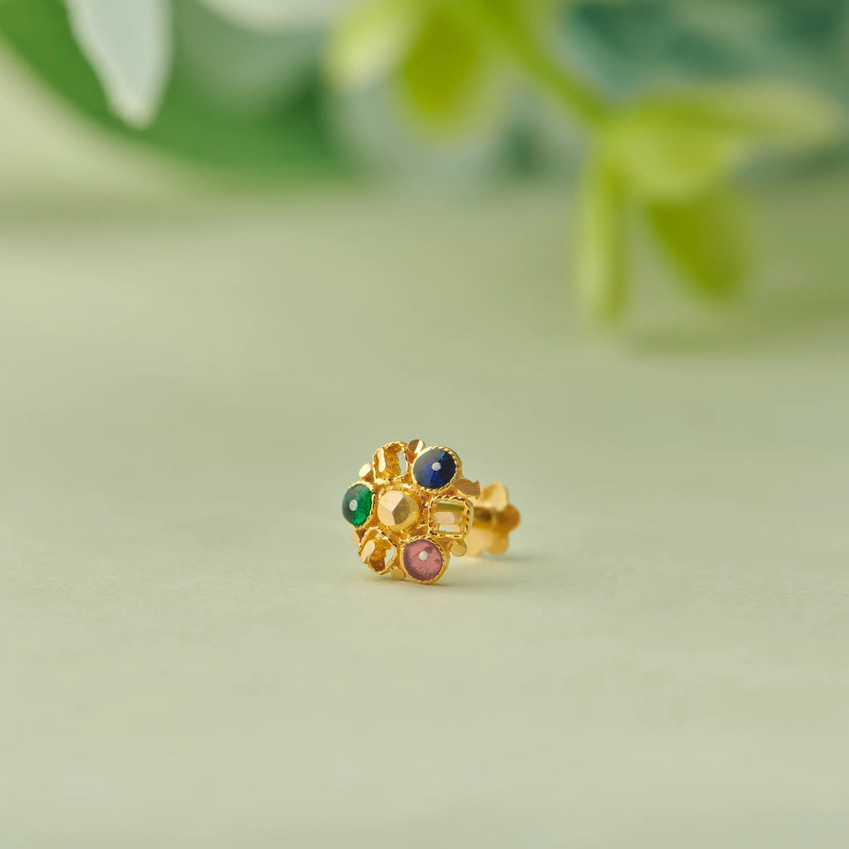 Close up of multicolour stone floral gold nose pin placed on a soft green background highlighting fine detailing