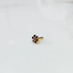 A gold flower-shaped nose pin with oval-cut multicolor stones in teal, red and purple, placed on a white background