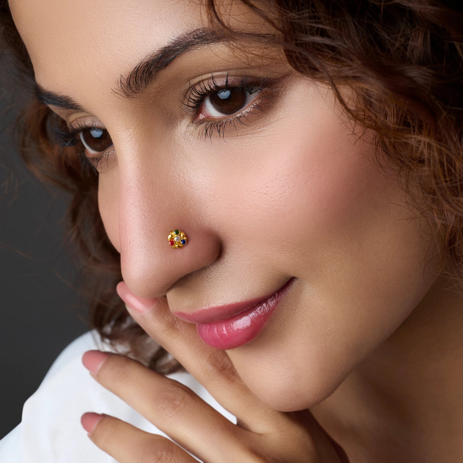 Woman wearing a round gold nose pin with multicolor stones