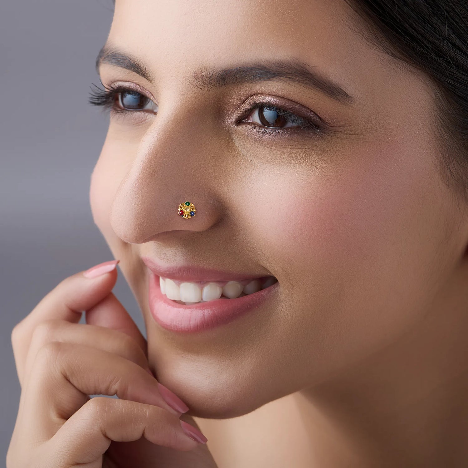 Close-up of a smiling woman wearing a gold flower nose pin with colorful gemstones