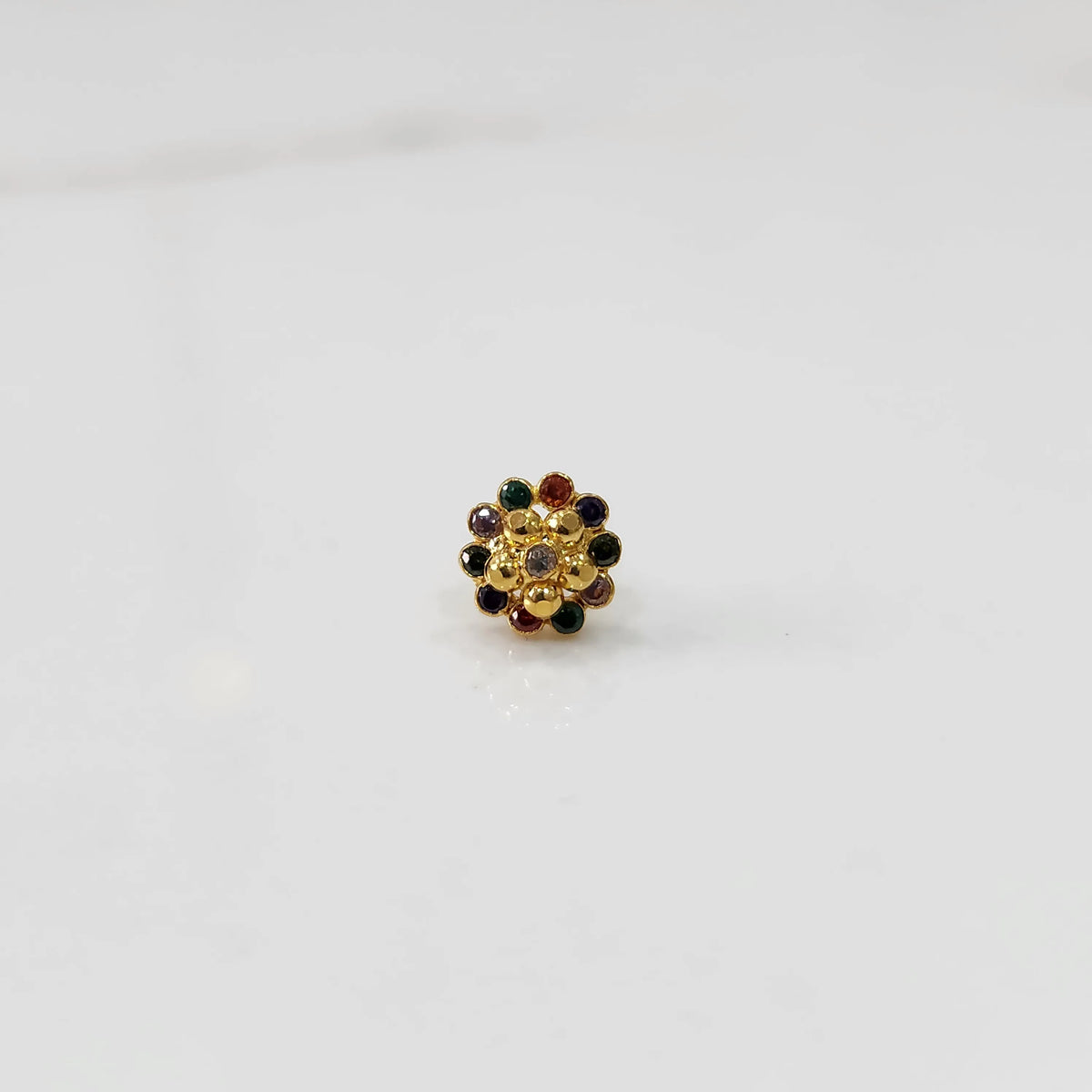 Top view of gold floral nose pin with navratna multicolor stones