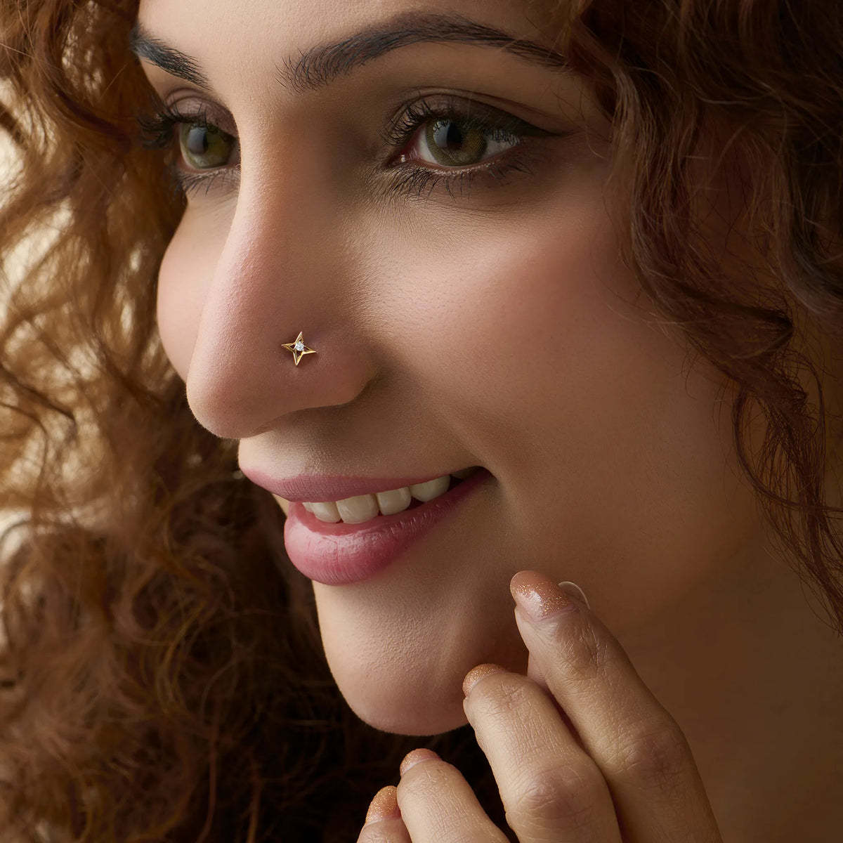 Gold star diamond nose stud worn by a smiling woman, close-up beauty shot