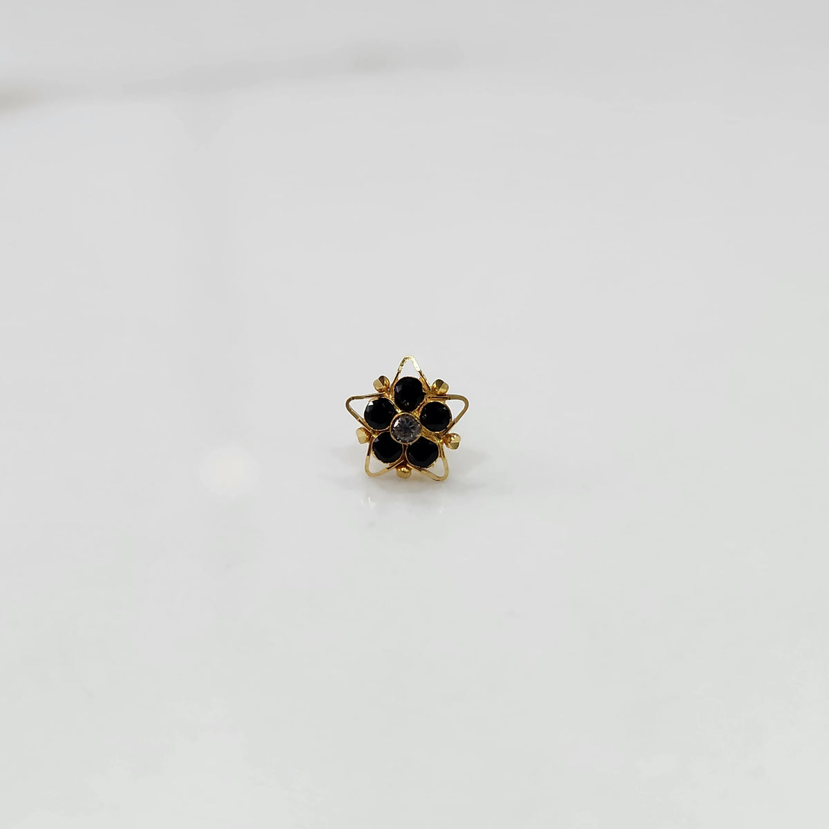 Nose pin design gold with black floral gemstone cluster on white background