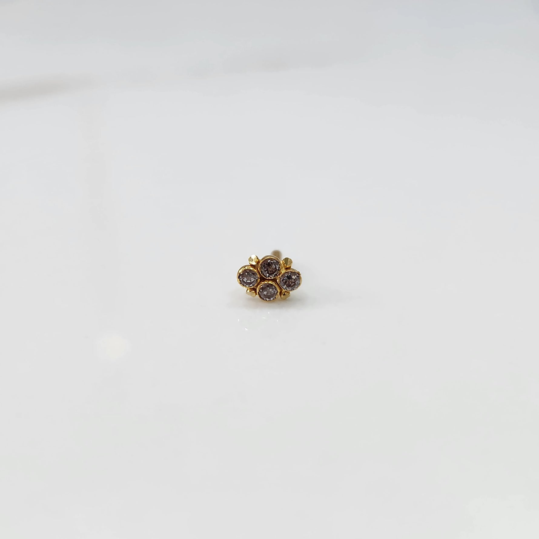 Women's gold nose pin design with subtle diamond floral cluster on white background