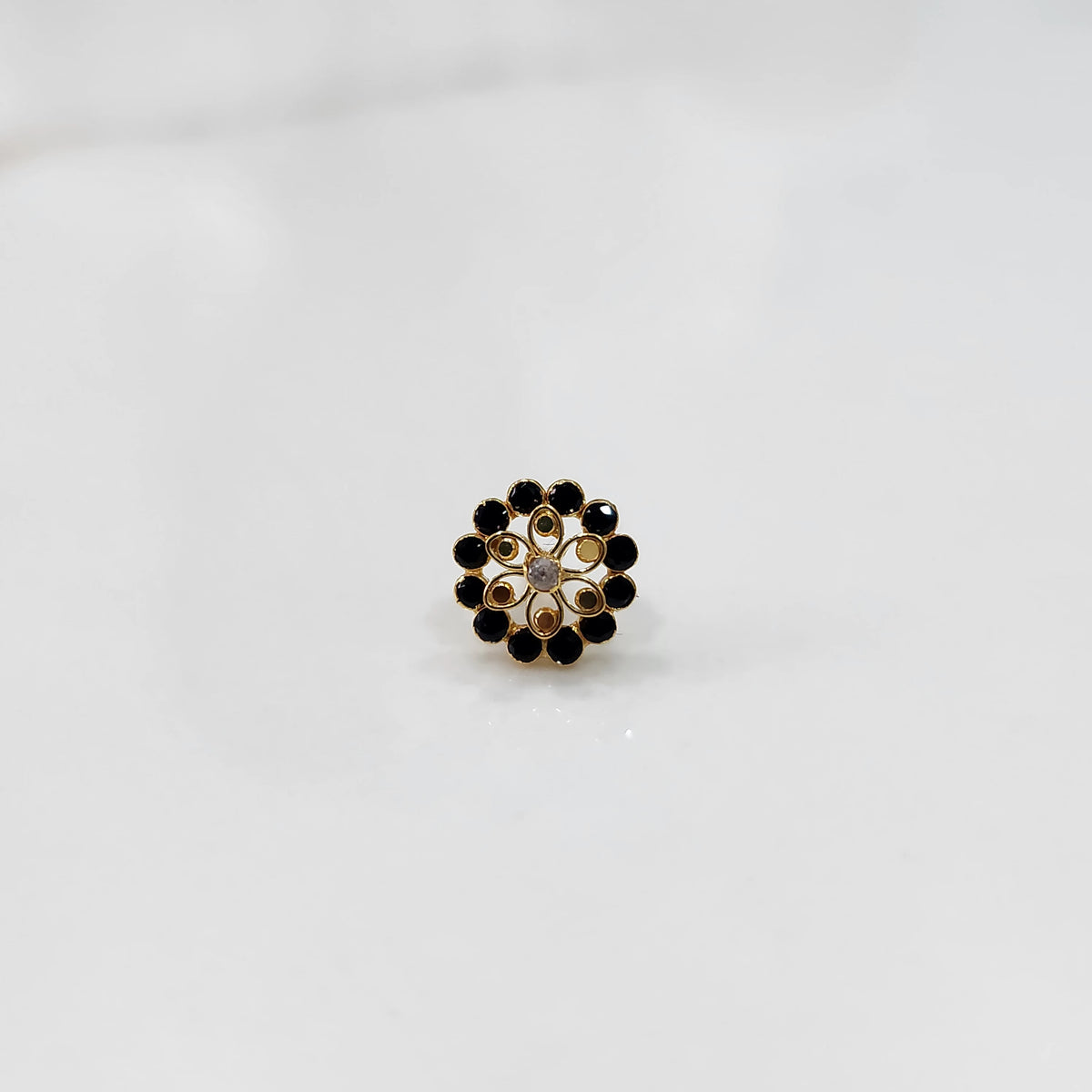 Gold nose pin design with black stone floral cluster on white background
