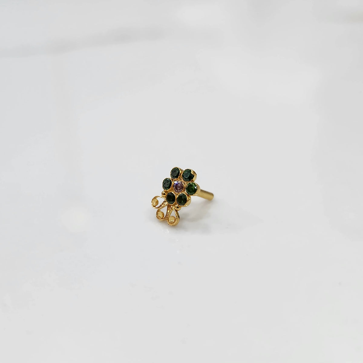 Gold nose pin featuring green floral cluster with purple accent and ornate curling detail