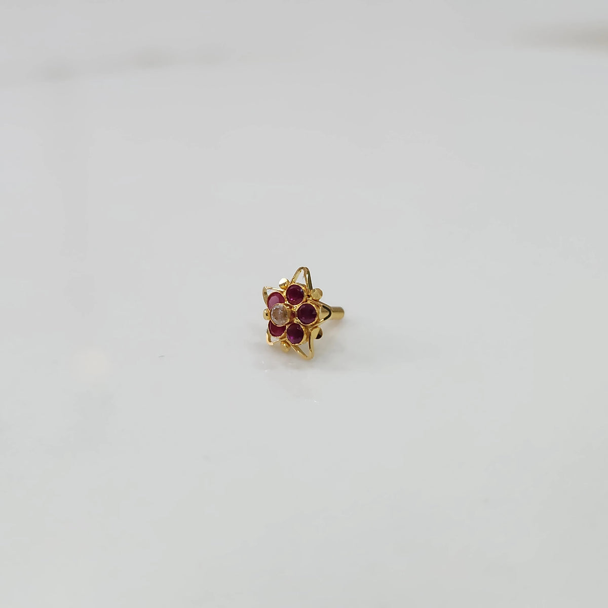 Gold nose pin featuring six-point star design with ruby and champagne stone cluster