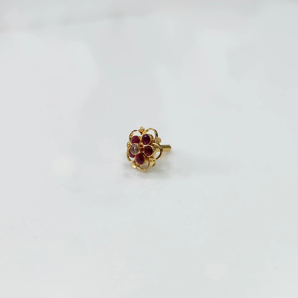 Gold floral nose pin with ruby stones and scalloped swirl border