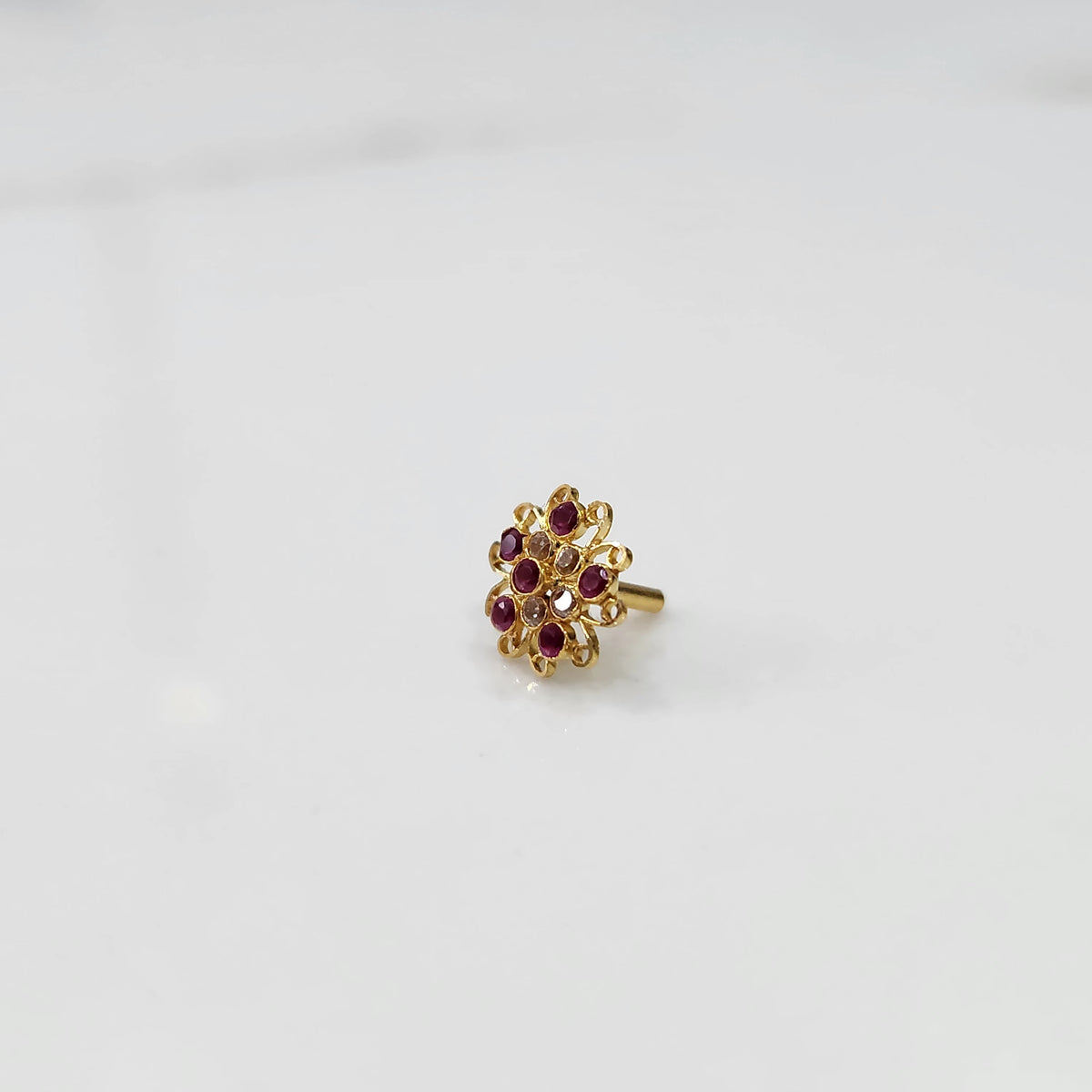 Gold nose pin with ruby round-cut stones and ornate swirl border