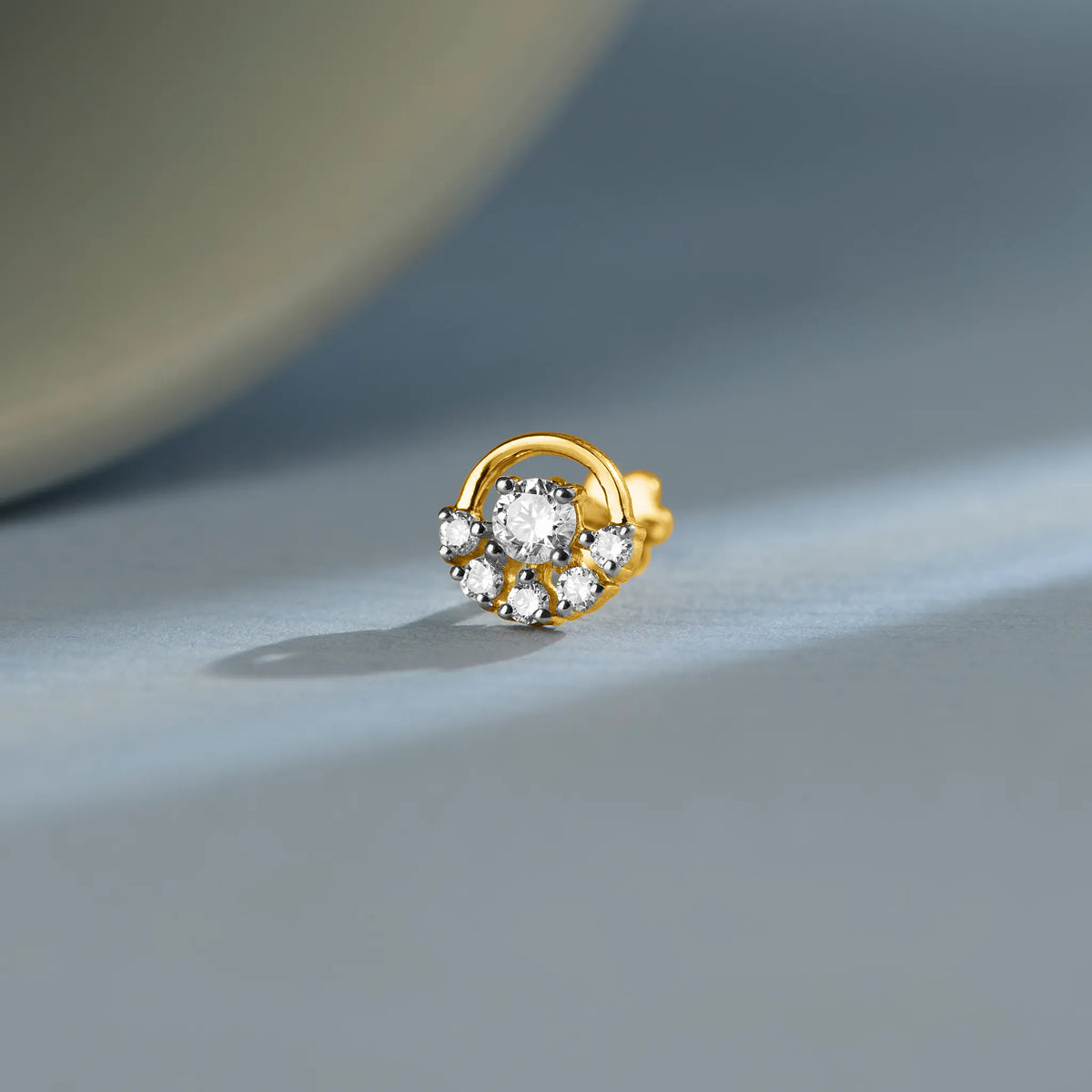 Round floral gold nose pin design with center diamond and halo setting on soft background