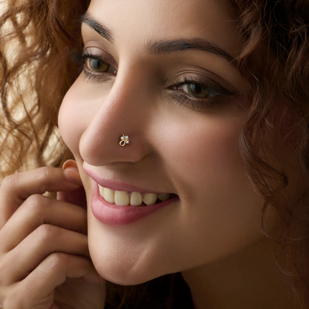 Smiling woman wearing a delicate gold nose pin with a shiny stone on her nose.