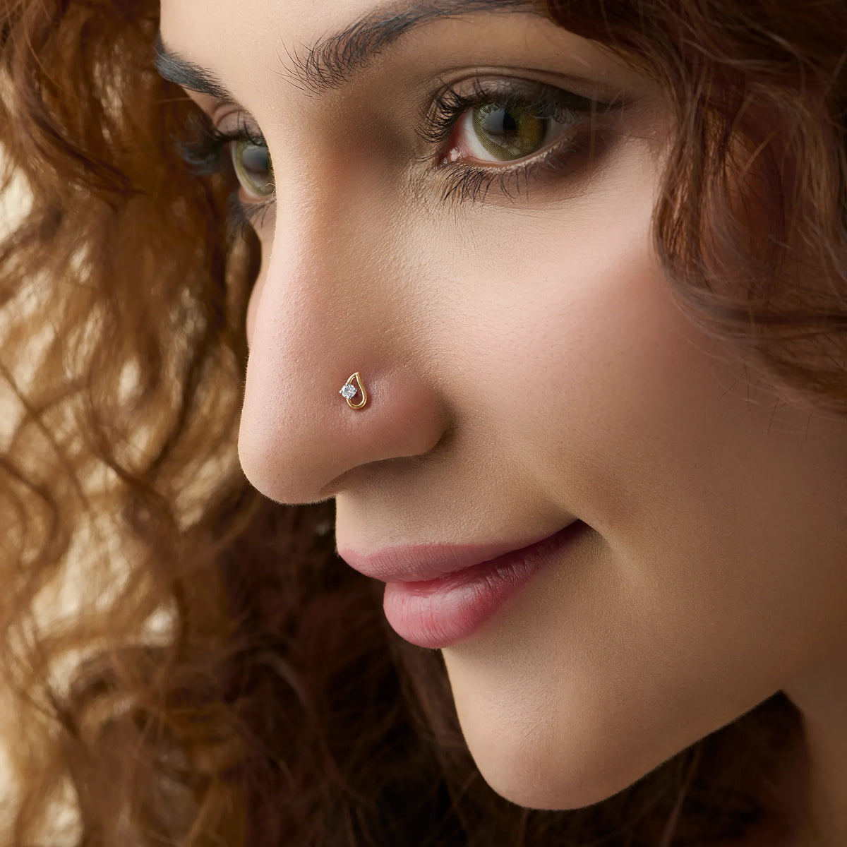 Side profile of a woman wearing a small gold nose pin with a shiny stone on her nose.