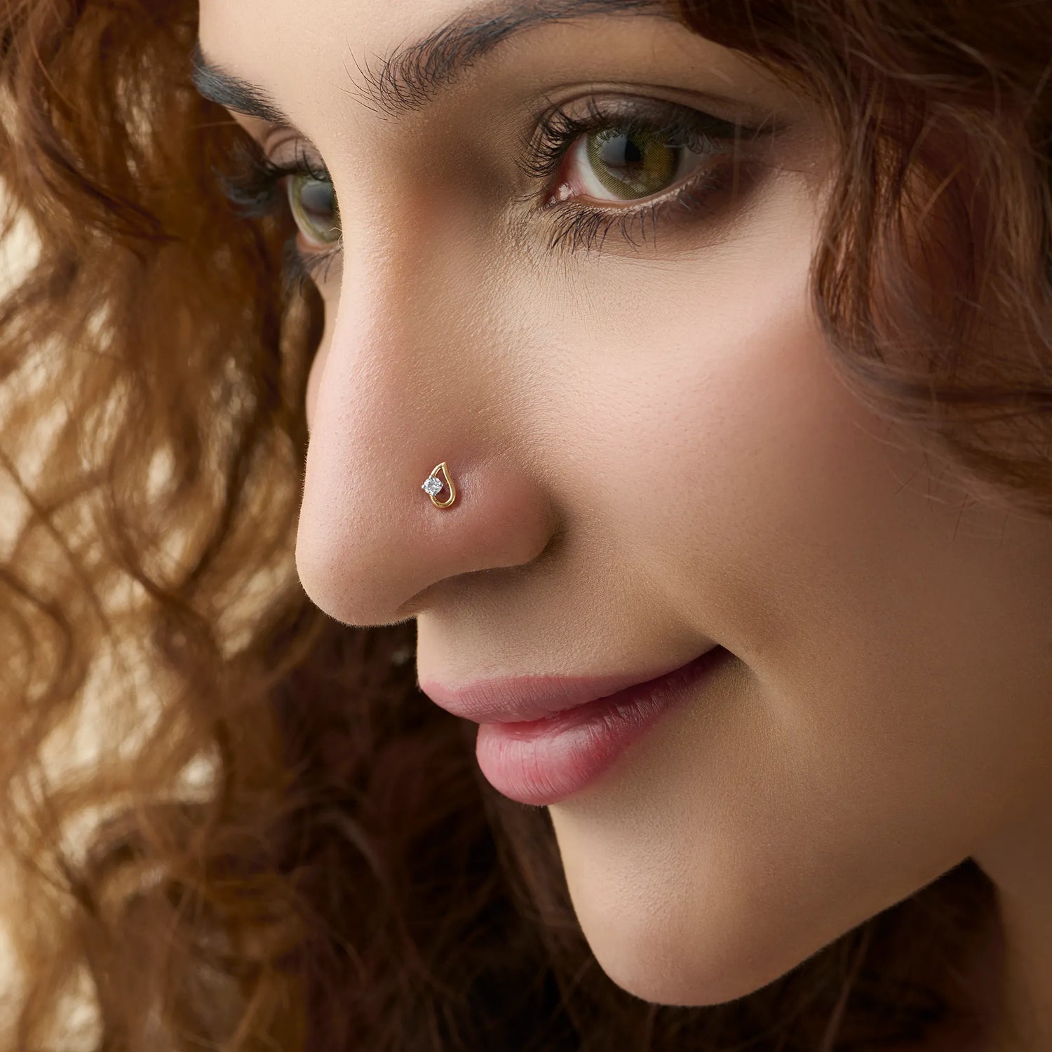 Side profile of a woman wearing a small gold nose pin with a shiny stone on her nose.
