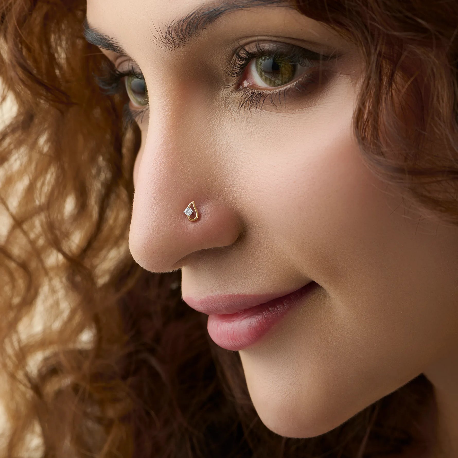 Side profile of a woman wearing a small gold nose pin with a shiny stone on her nose.