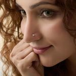 Close-up side profile of a woman wearing a delicate gold flower nose pin with a shiny stone.