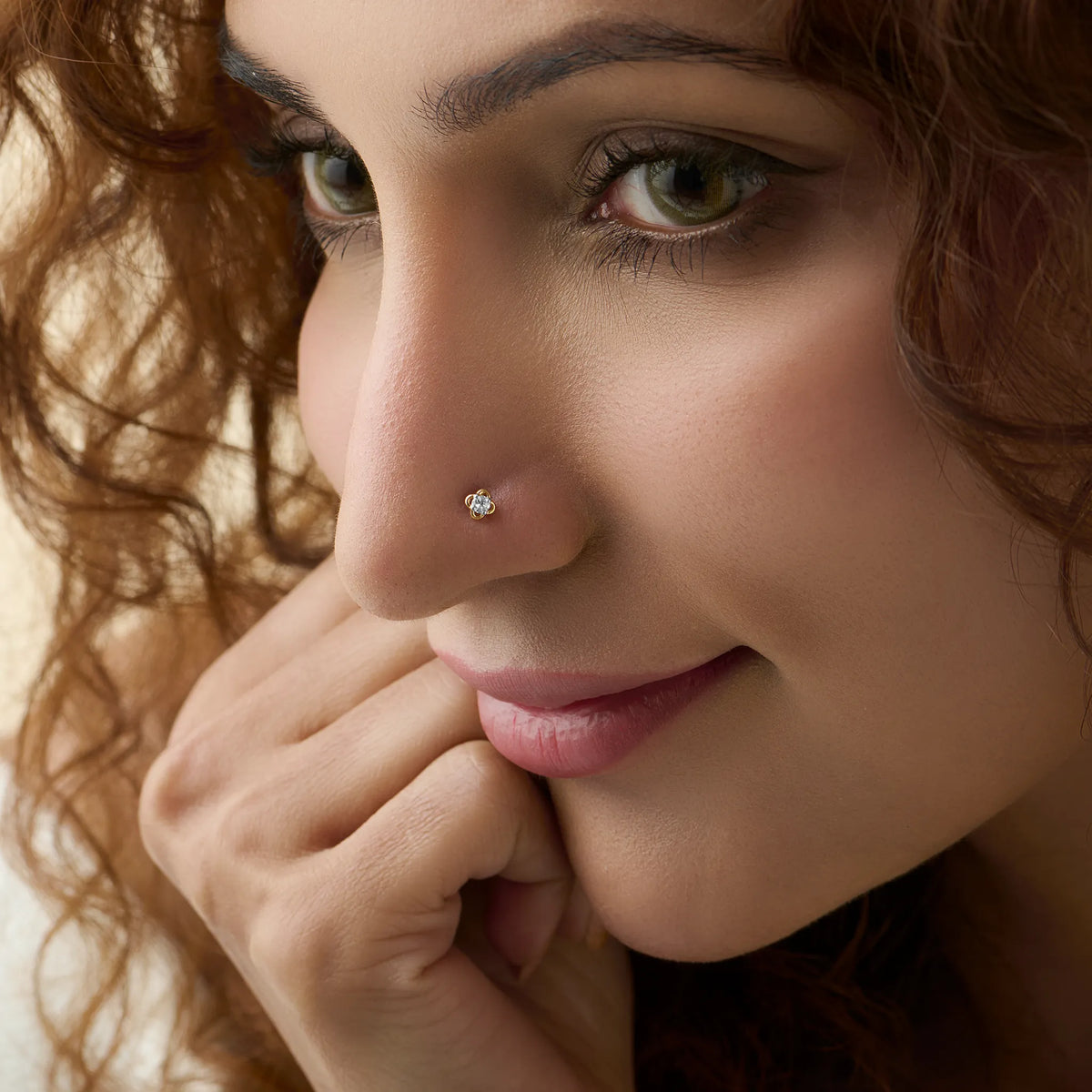 Close-up side profile of a woman wearing a delicate gold flower nose pin with a shiny stone.