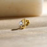 Close-up of a gold stone nose pin with a sparkling white gemstone placed on a soft beige surface.