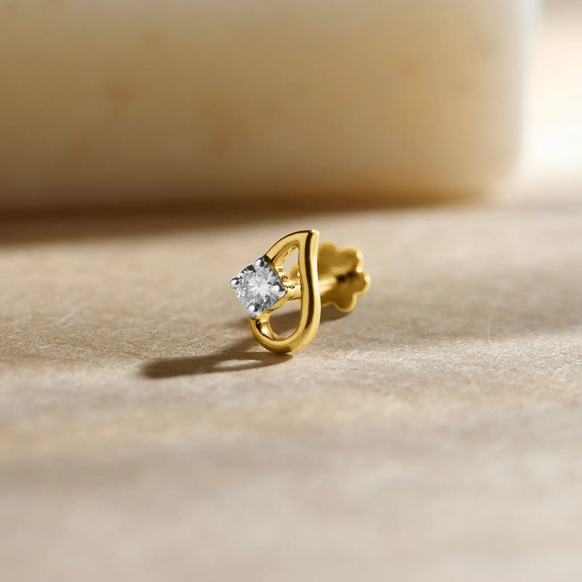 Close-up of a gold stone nose pin with a sparkling white gemstone placed on a soft beige surface.