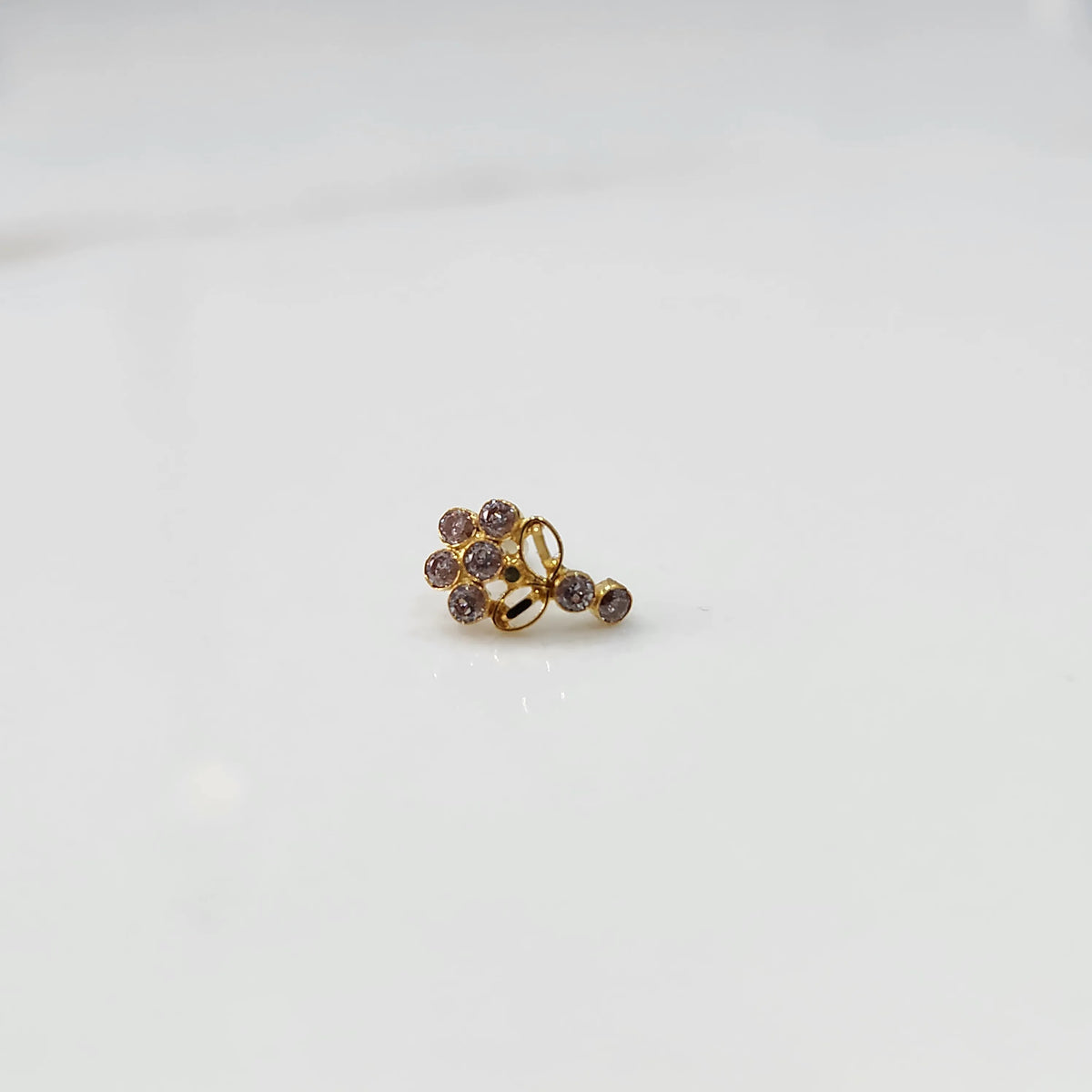 Angled view of gold nose pin with pink gemstone cluster and clear drop-style stone accent on white background