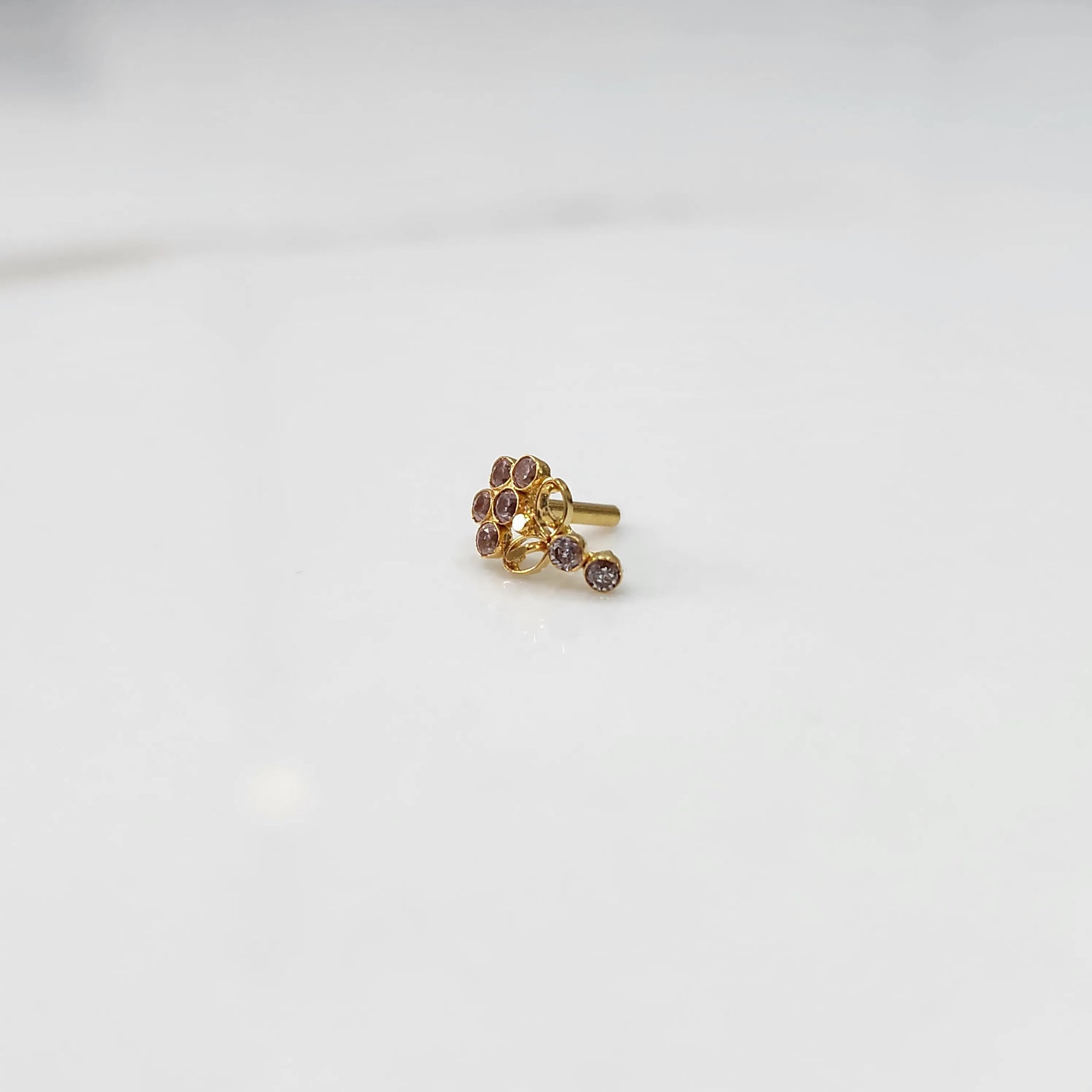 Gold nose pin with pink gemstone cluster and clear drop-style stone accent on white background