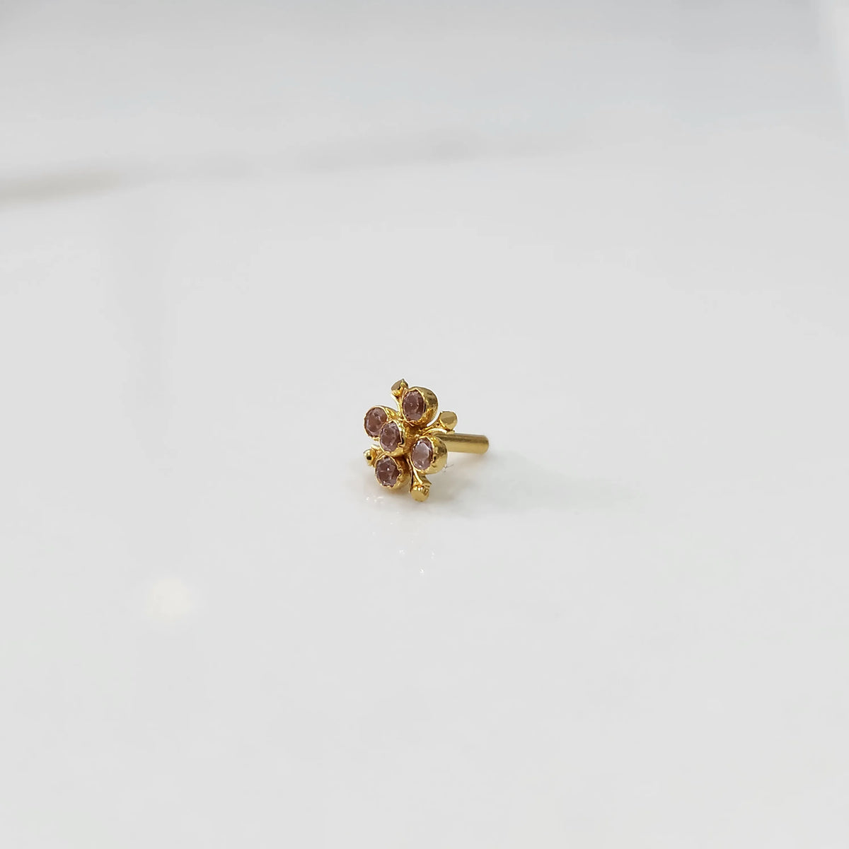 Gold nose pin with pink gemstone flower cluster on white background