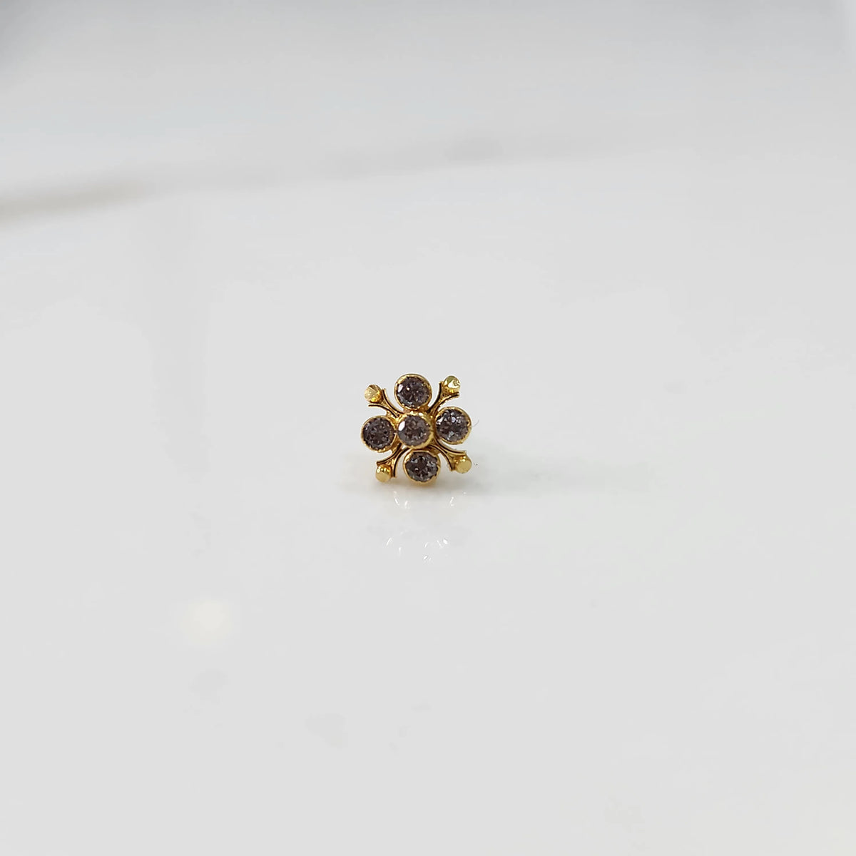Front view of gold nose pin with pink gemstone flower design on white background