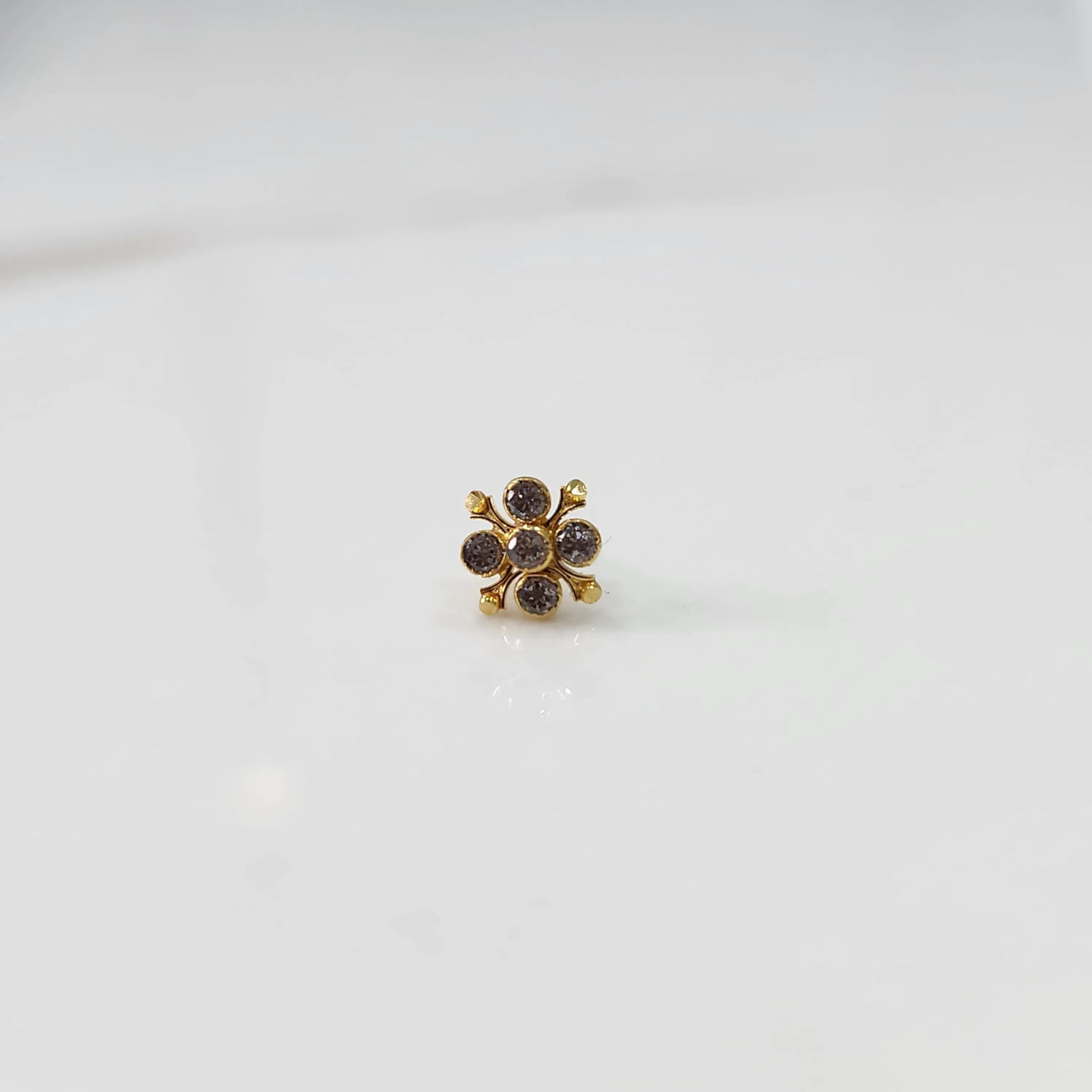 Front view of gold nose pin with pink gemstone flower design on white background