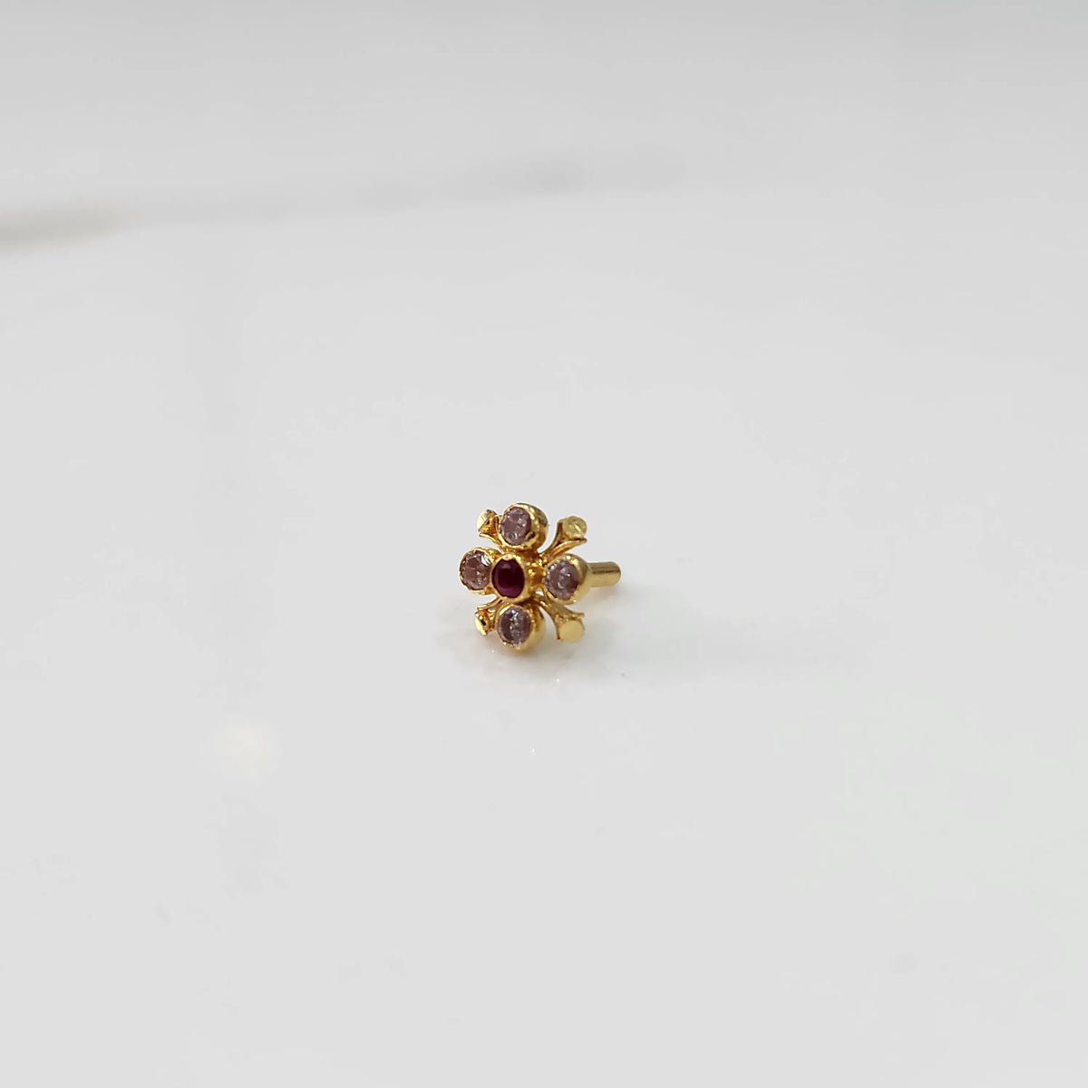 Gold nose pin with pink gemstone petals and red center stone, angled view on white background