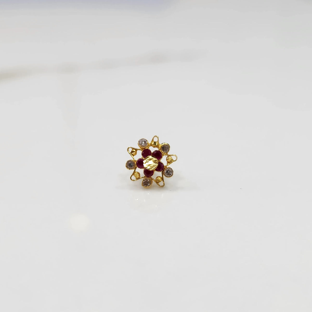 Close-up of gold ring featuring red and clear round gemstones