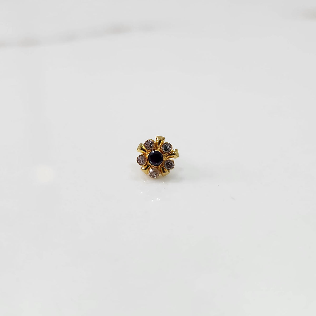 Gold floral nose pin with purple center stone, product shot