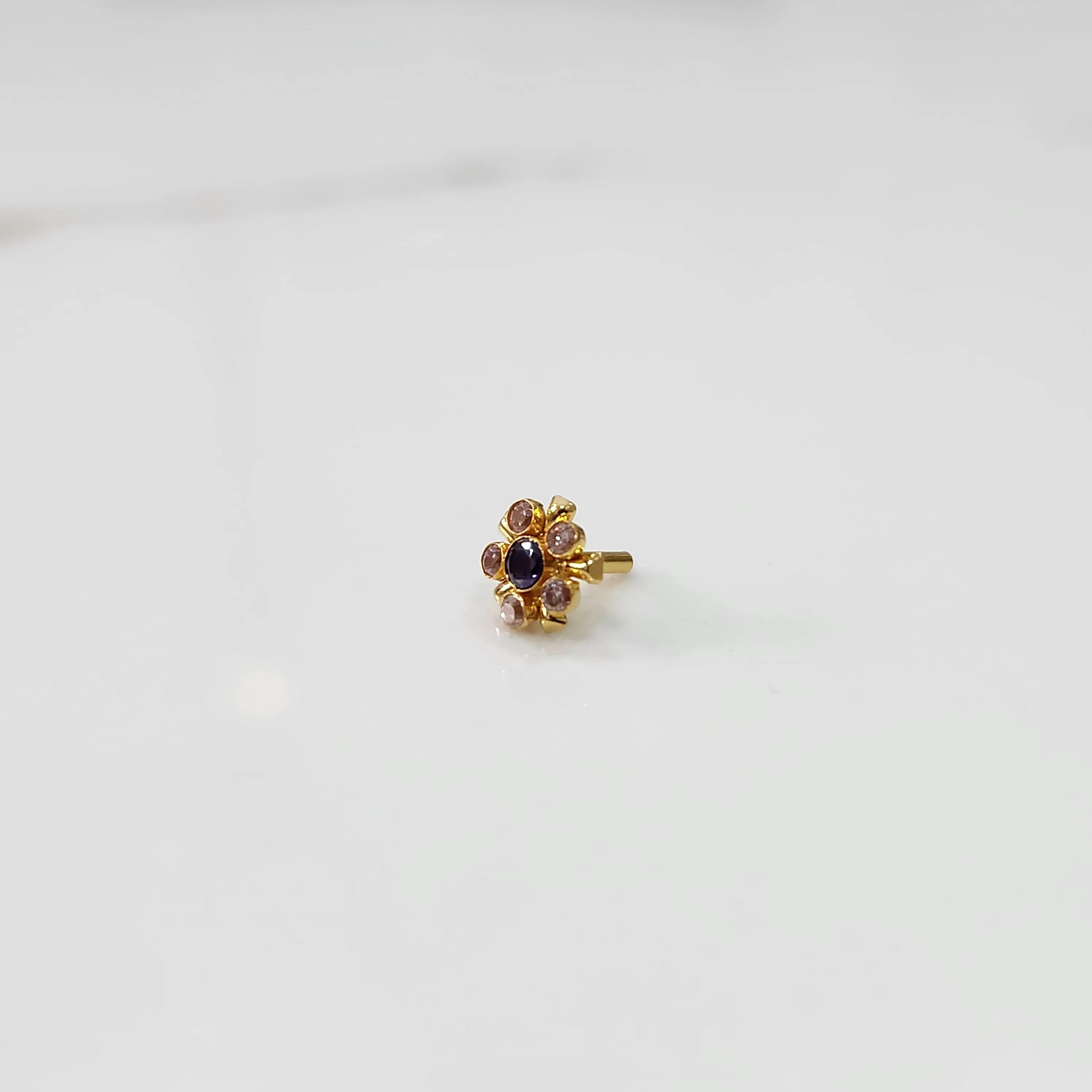 Close-up of flower-shaped gold nose pin with mixed stone colors