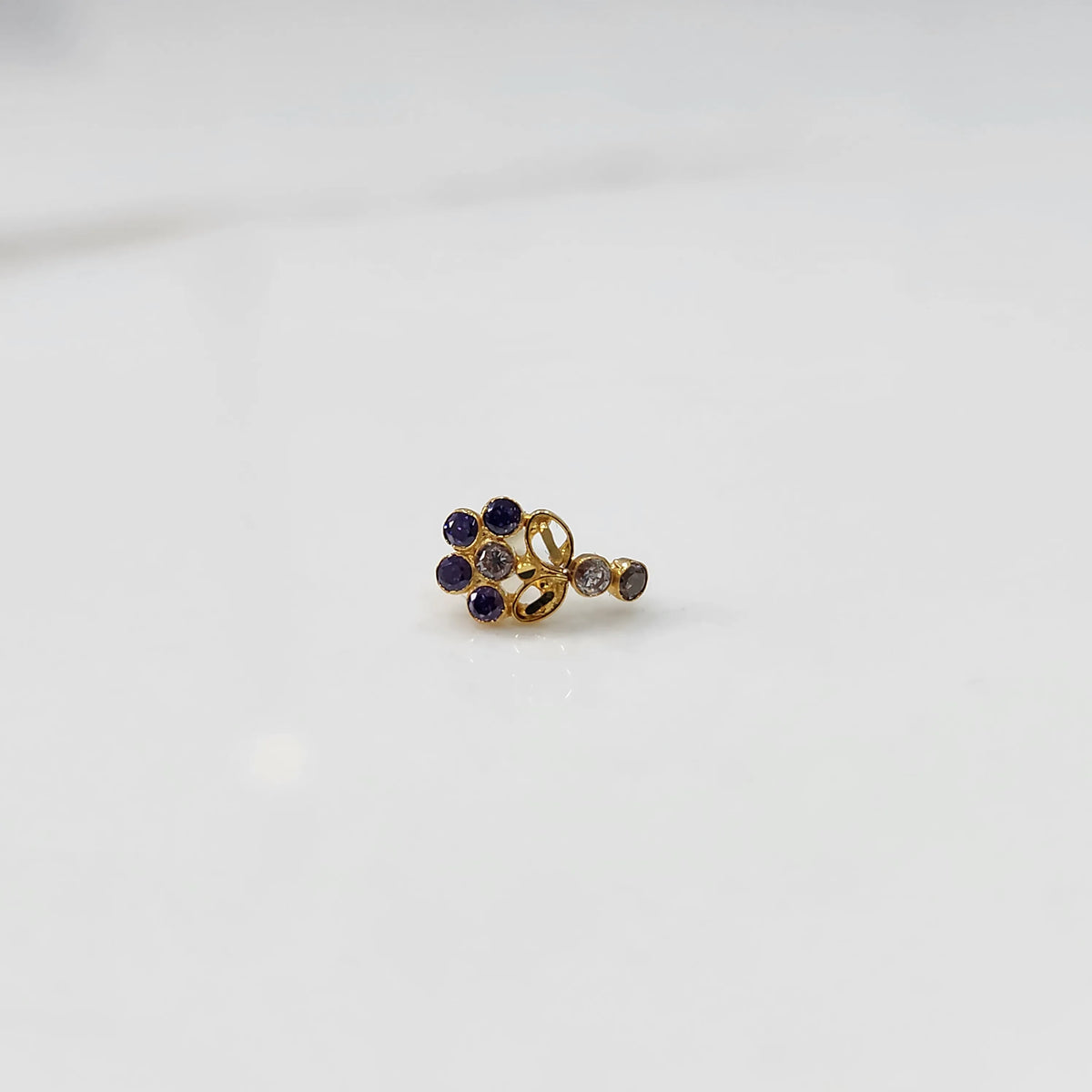 Gold nose pin with purple gemstone cluster and clear drop-style stone accent on white background