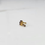 Front view of gold nose pin with purple gemstone cluster and clear drop-style stone accent on white background
