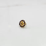 Close-up of flower-shaped gold nose pin with purple gemstone border