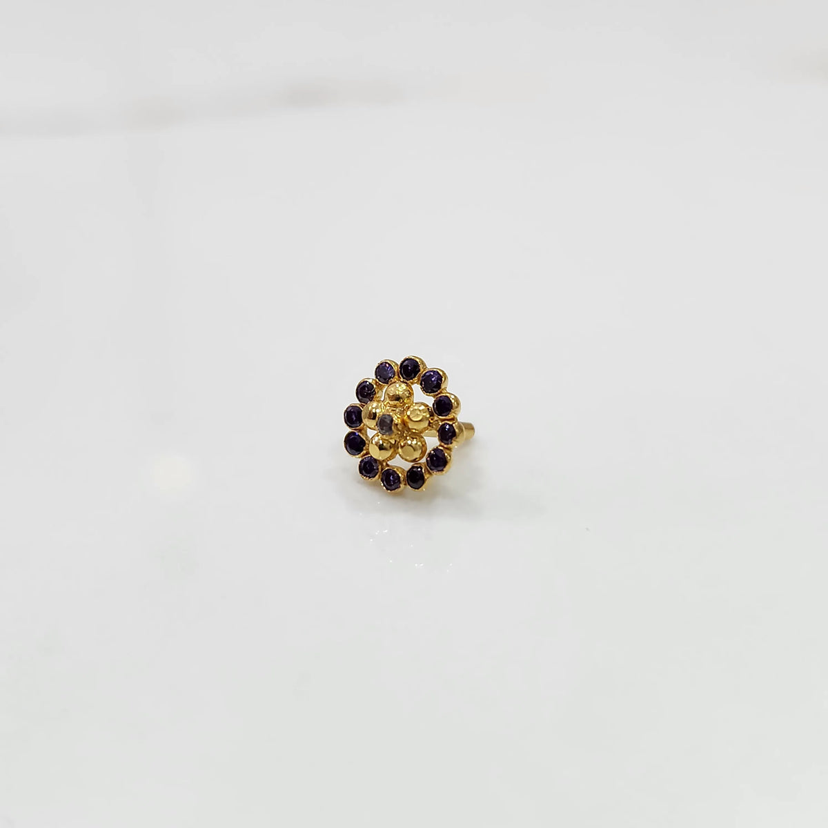 Close-up of flower-shaped gold nose pin with purple gemstone border