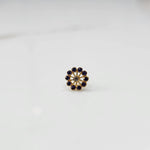 Front view of large gold nose pin with purple gemstone petals and clear center stone on white background
