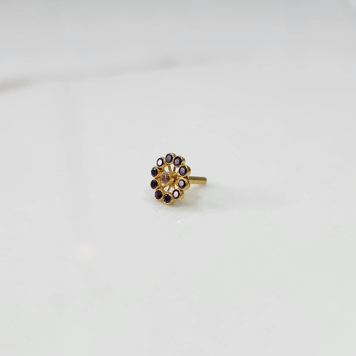 Large gold nose pin with purple gemstone petals and clear center stone on white background