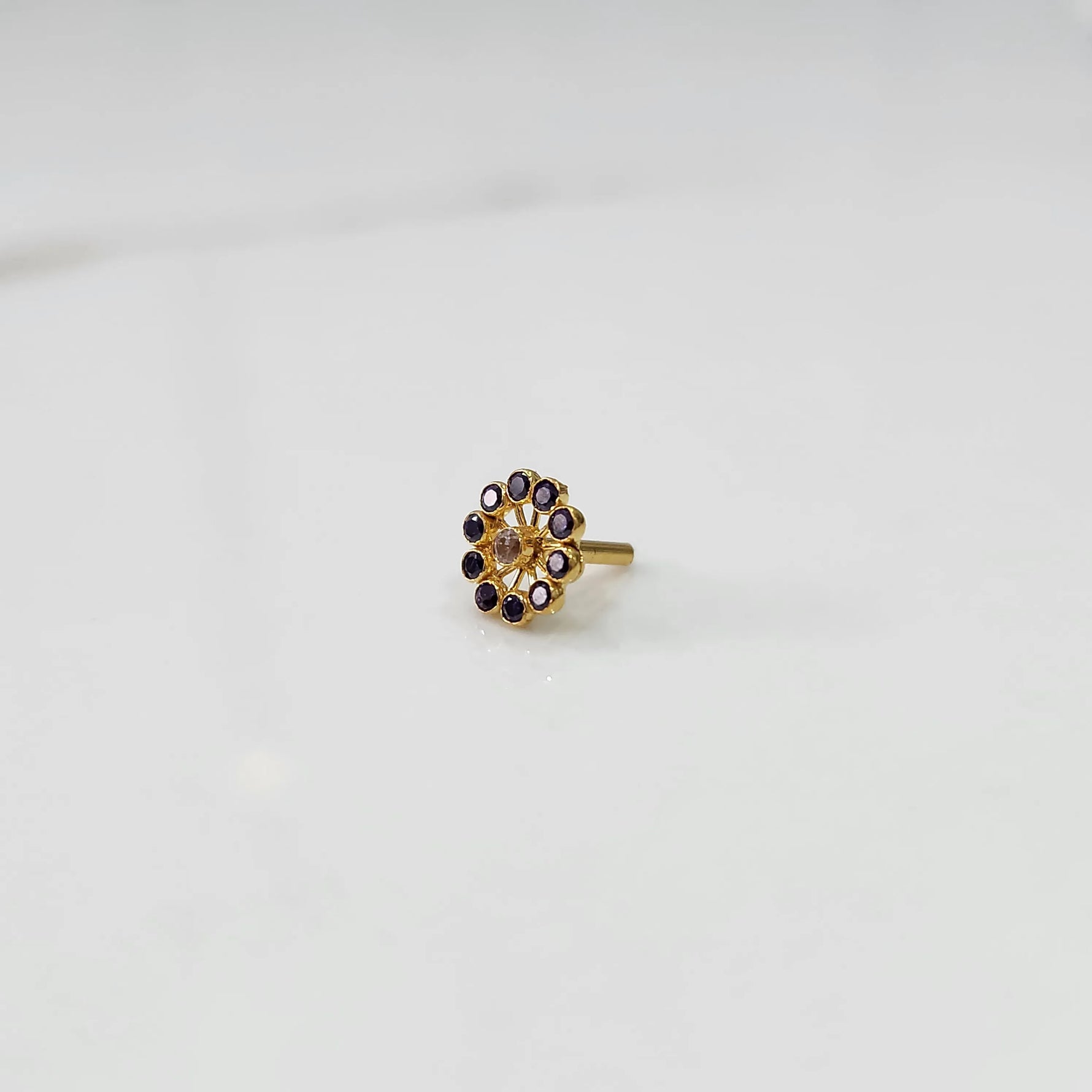 Large gold nose pin with purple gemstone petals and clear center stone on white background