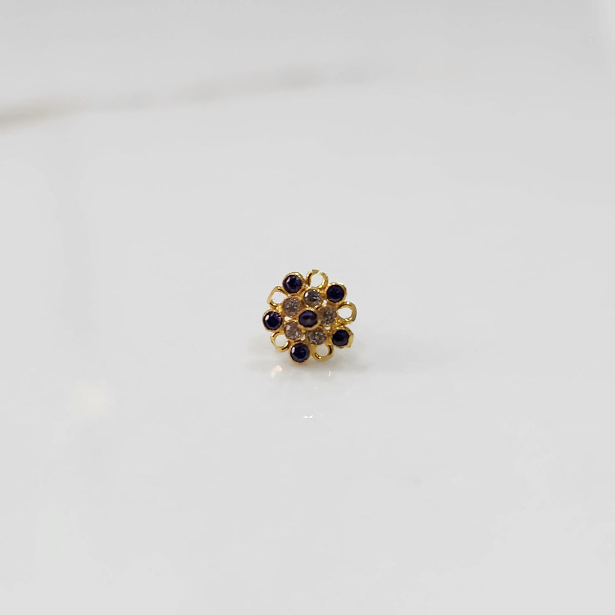 Front view of gold nose pin with purple gemstone mandala design on white background