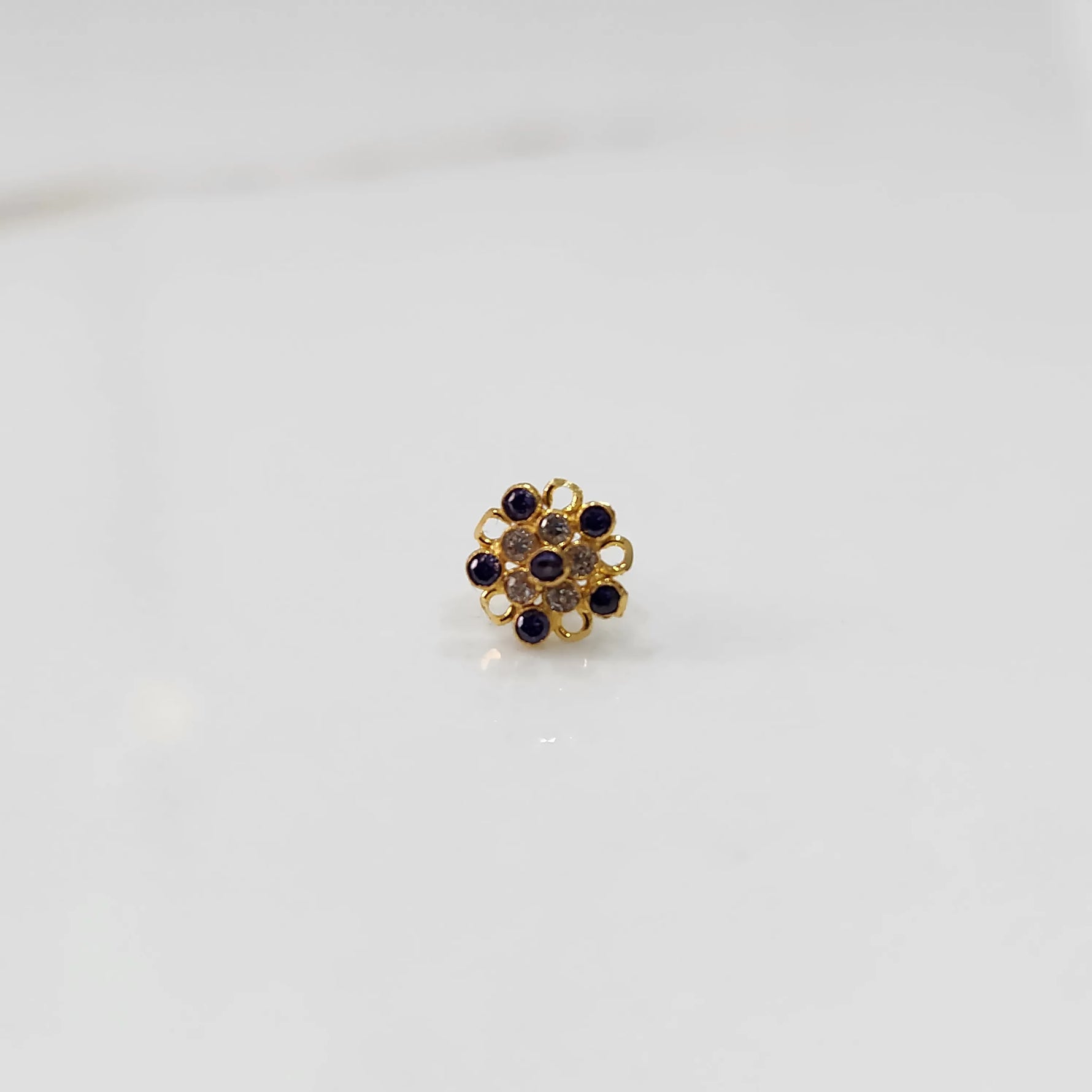 Front view of gold nose pin with purple gemstone mandala design on white background