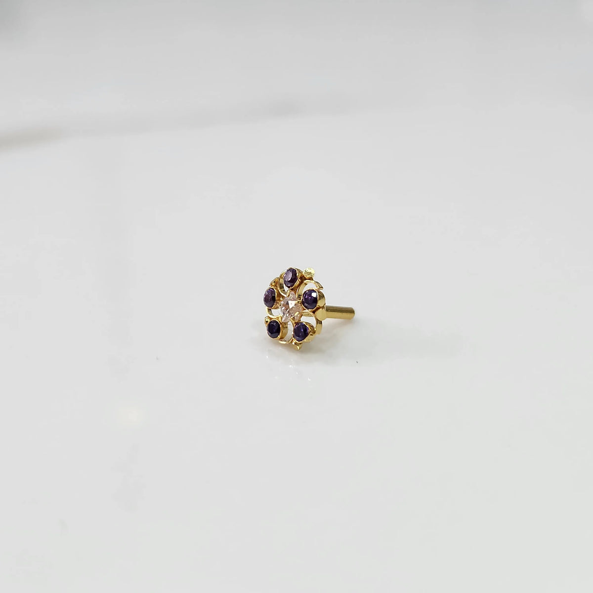 Gold nose pin with purple gemstone petals and clear center stone on white background