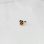 A gold flower-shaped nose pin with purple stones around a small white center stone, placed on a white background