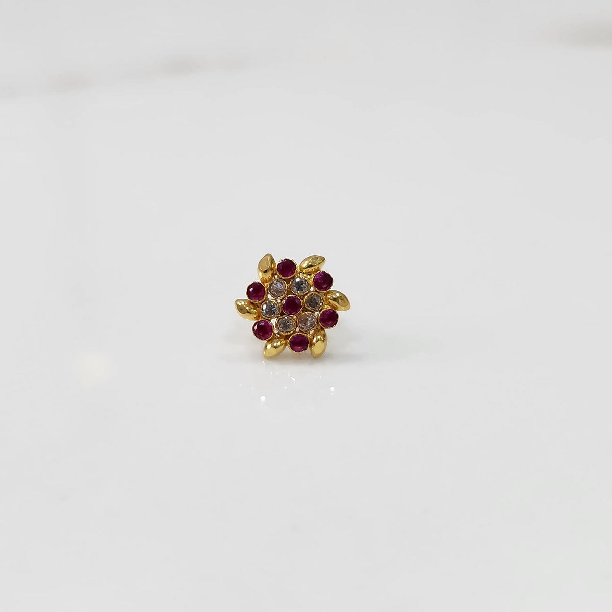 Front view of gold statement ring with red and clear gemstones in leaf-patterned cluster design