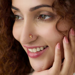 Woman wearing gold drop-style nose pin with red stones