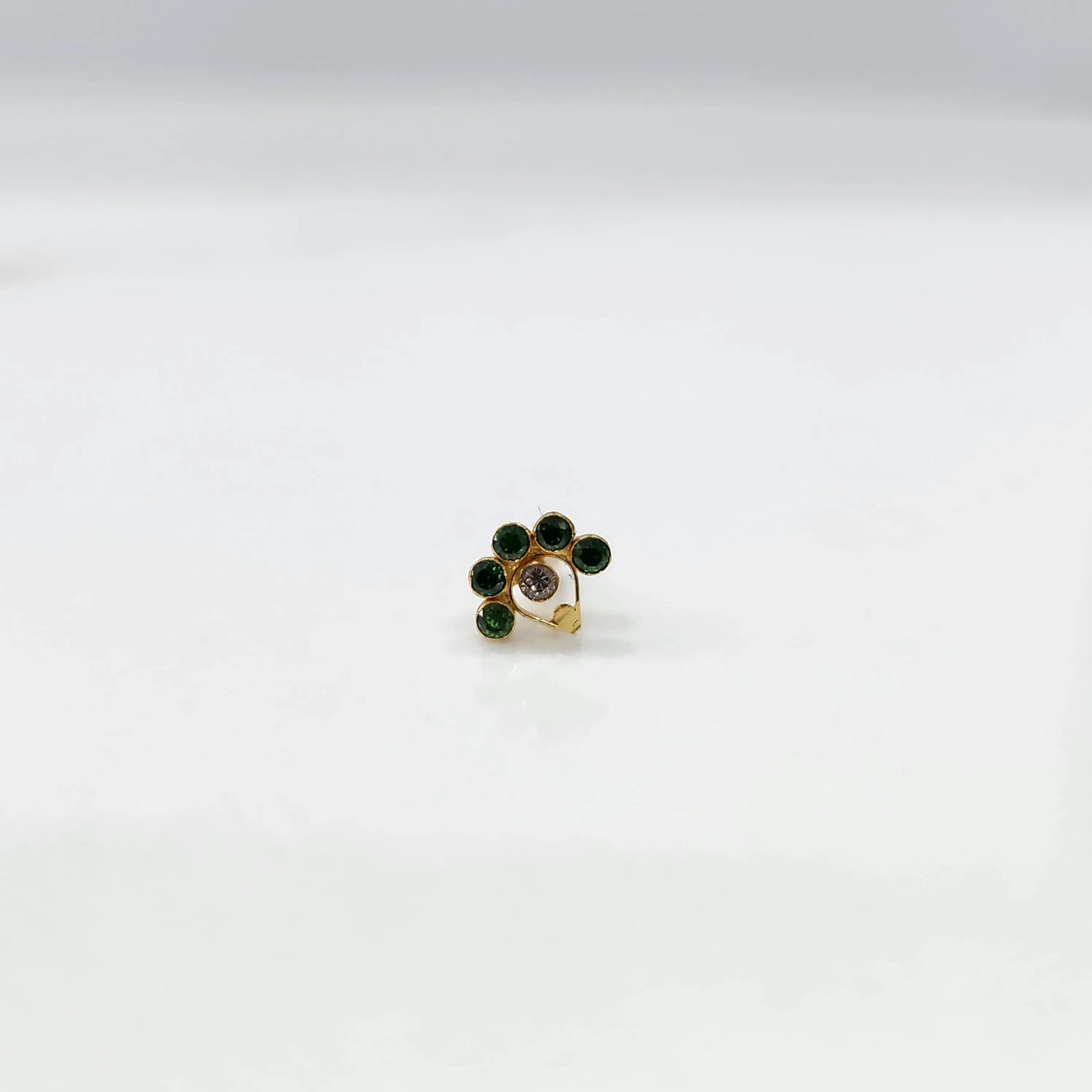 Front view of gold ring featuring green floral gemstones with clear center and drop pendant
