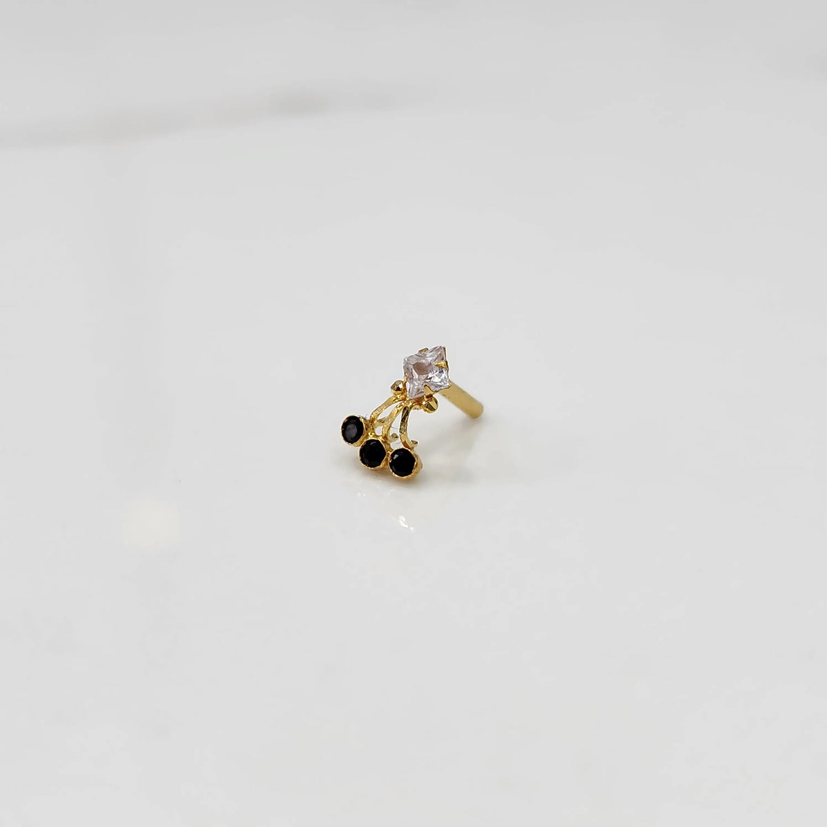 Side view of gold ring with square clear stone and black gemstone drop design