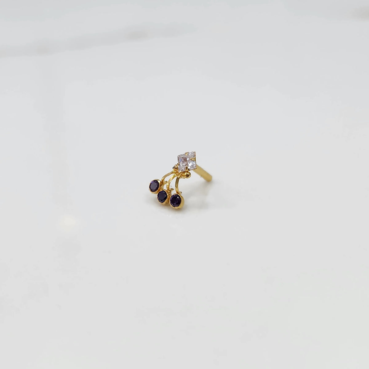 Gold ring with square clear stone and purple gemstone drop design