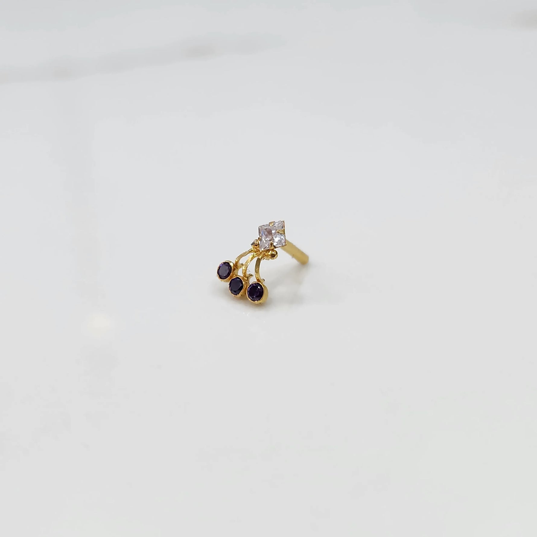 Gold ring with square clear stone and purple gemstone drop design